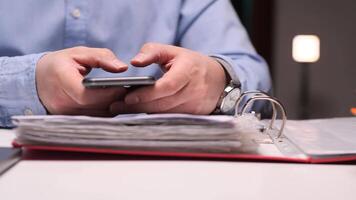 Office worker browsing smartphone with documents and files in background video