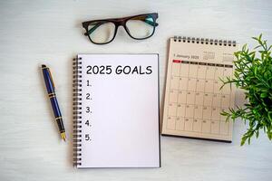2025 New Year goal, plan, and action concepts. 2025 goals Text on Note Pad with calendar, glasses on the table.New Year's resolutions plan.Happy New Year theme, top view photo