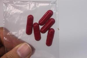 A person holding up four red pills in a plastic bag photo