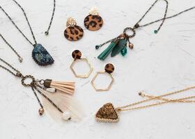 Boho style jewelry handmade set, golden earrings and necklaces with gems and feathers, lying flat on the white plaster background, top view with empty place for your text photo