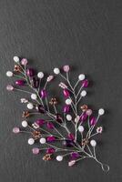 Beautiful handmade crafted embellishment, purple branch with beads and crystals, lying flat on the dark gray stone rectangular background, vertical top view photo