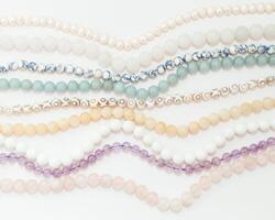 Set of threads different semiprecious gemstones beads in light pastel colors,pink quartz,white agate,pearls,jade,violet amethyst,greenstone and turquoise on the white background,top flat lay view. photo