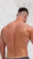 Muscular sportsman without t-shirt in nature. Back-side view of a strong man on white mountain background. Close-up. Vertical video