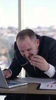 Man doing funny faces sitting in front of laptop. Mad businessman typing nervously with fingers on keyboard and looking to the sides. Entrepreneur with insane face in office. Vertical video