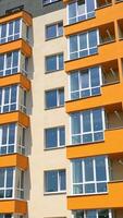 Modern high rise building with glazed balconies. Front view of newly built block of flats with colorful walls. New apartment building facade in the city. Vertical video