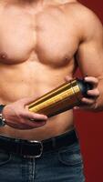 Topless athlete with flask. Muscular body of a sportsman isolated on red studio background. Healthy man's body with trained biceps. Close-up. Vertical video
