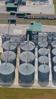 New industrial complex with grain silos. Grain storage tanks in the countryside. Modern grain-drying farm with large silver terminals in rural landscape. View from above. Vertical video