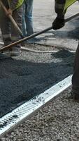 A man uses a shovel to lay asphalt near a drain to divert water. video