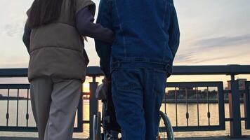 A young family of three, including a child with special needs, enjoys the beautiful view of the evening sunset from the city embankment. video