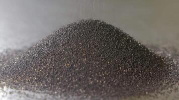 Dark synthetic diamond abrasive powder forming a dense pile on metallic surface, Macro close-up showing raw material used in heavy-duty cutting and grinding applications video