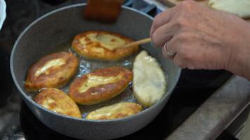 Grandma's hands turn over fried pies in a frying pan in boiling oil. Pie fried, food from homemade dough. video