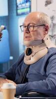 Vertical Medical staff consults old man wheelchair user wearing cervical neck collar, taking fever measurements with a thermometer. Expert consultation in disability friendly cabinet. Camera B. video