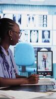 Vertical African american nurse making a videocall with doctor to chat with patients, doing a remote check up and telemedicine concept. Skilled medical assistant asks opinion of a specialist. Camera A. video