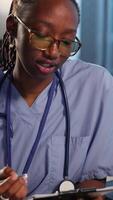 Vertical African american nurse evaluating lab test results and creating a recovery plan with elderly couple, professional patient interaction at the facility. Examination results and analysis. Camera B. video