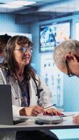 Vertical Female physician and ill patient reviewing hospital records papers at checkup, doing scan interpretation of x ray results. Medic specialist emphasize healthcare practices and research. Camera A. video