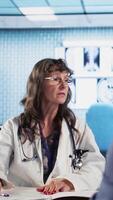 Vertical Healthcare specialist sharing medical expertise and reading the MRI scans results with male patient, reviewing x ray reports for the correct diagnostic. Expert discuss treatment plans. Camera A. video