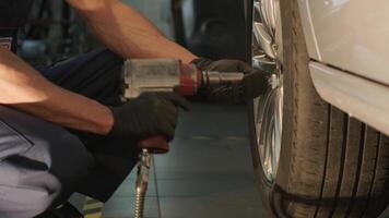 Technician changing car tire using impact wrench at repair station. video