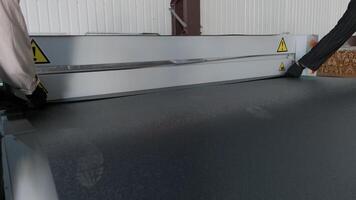 Worker operating a sheet metal feeding system with black-coated steel under active processing. video