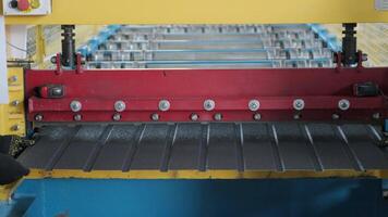 Corrugated sheet metal emerging from a red and yellow roller machine during shaping process. video