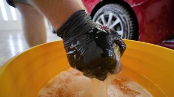 Auto detailer squeezing sponge soaked with soapy water from orange bucket. video