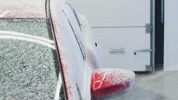 Red car partially covered in white foam during the pre-wash stage in detailing bay. video
