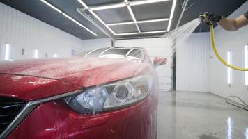 Front of red vehicle covered in foam during pressure washing session. video
