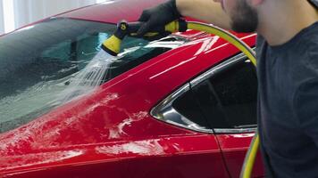 Worker rinsing off shampoo from red car using hose with high-pressure water. video