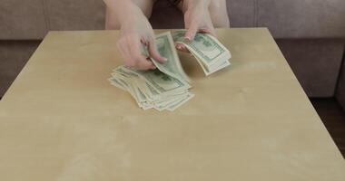 Hands carefully sort and count stacks of US dollar bills on smooth wooden table in well lit indoor space focus is on currency being handled video