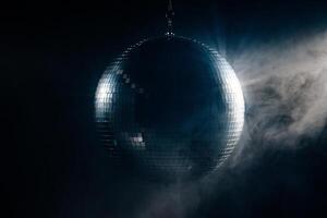 Disco ball with mirror surface in backlight. Bright rays, smoke, hanging on ceiling, night party background photo