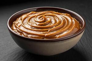 Close-up of a bowl of dulce de leche forming waves on top on black background - generated by ai photo