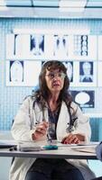 Vertical Senior doctor and patient discussing diagnostic results in modern medical office, showcasing advanced technology using computer displaying x rays and MRI scans. Care management. Camera A. video