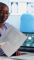 Vertical African american assistant and patients engage in medical checkup with hospital records and x ray results files to find accurate treatment for wellness and recovery. Healthcare practices. Camera B. video