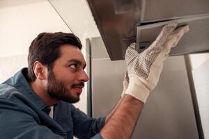Handyman in uniform repairing kitchen extractor, replacing filter in cooker hood.Maintenance concept photo