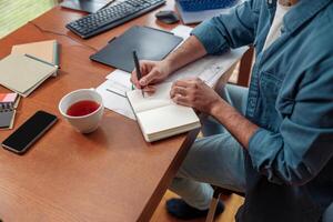 Close up of man hands making notes in notepad while sitting on his workplace photo
