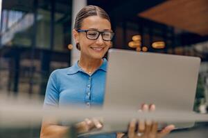 A Happy Smiling Woman is Using a Laptop in a Modern Workspace Setting for Work Purposes photo