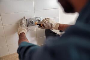 Close up of professional electrician worker with screwdriver is repairing power socket in kitchen photo