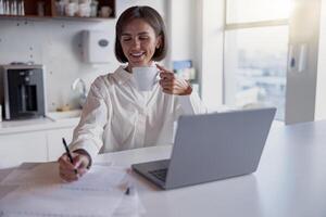 Charming business woman working at the office using laptop and making notes while drinking coffee photo