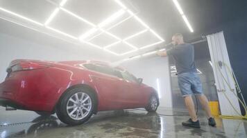 Red sedan being washed under bright workshop lights. video