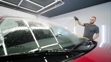 Auto detailing technician working on front of car with foam. video