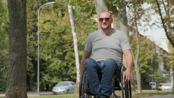 Smiling man with a disability in a wheelchair relaxing in a shaded park area. video