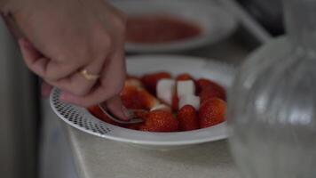 A red strawberry berry in a plate. Here's how you can make a light snack for dessert at home. A man's hand is kneading strawberries in a plate with a fork. video