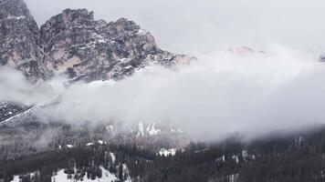 Aerial view of rugged Dolomite peaks near Cortina, with snow covered slopes, sparse trees, and misty clouds in a slow, sweeping pan. video