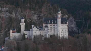 Aerial view of Neuschwanstein Castle surrounded by rugged mountains and bare trees. The camera moves smoothly, revealing details at sunset. video