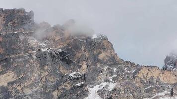 Aerial view of rugged Dolomite mountains near Cortina with rocky cliffs, drifting clouds, and gradual motion revealing dramatic textures. video