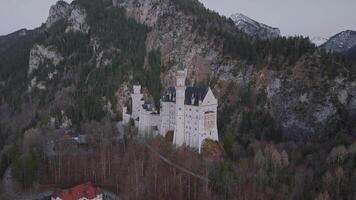 Aerial view of Neuschwanstein Castle in Bavaria, Germany, with snow capped mountains, dense forest, and a small church at sunset. Smooth camera motion. video