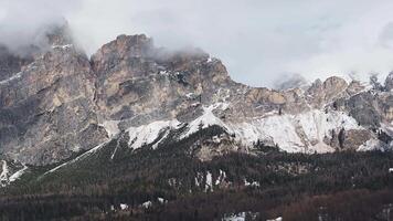 Aerial view of rugged Dolomite peaks near Cortina, with clouds, light, and shadow. The camera glides over steep cliffs and forested slopes. video