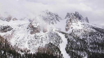 Aerial view of jagged Dolomite peaks near Cortina, partially shrouded in clouds, with evergreen forests on snowy lower slopes and smooth camera motion. video