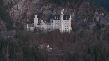 Aerial view of Neuschwanstein Castle surrounded by forests and cliffs, with snow capped mountains in the background and warm sunset lighting. video