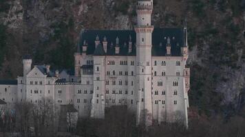 Aerial view of Neuschwanstein Castle with intricate spires, bare trees, and rocky mountains at sunset. Slow sweeping motion reveals dynamic perspectives. video