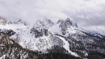 Aerial view of snow covered Dolomite peaks near Cortina, with clouds, coniferous forests, and smooth camera motion revealing the winter landscape. video